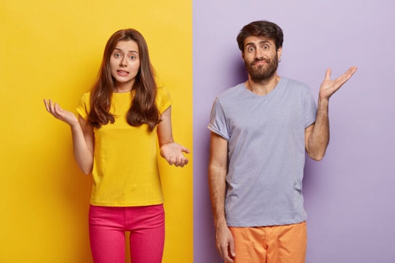 A woman and a man stand side by side against yellow and purple backgrounds, both shrugging with confused expressions, palms up. The woman wears a yellow shirt and pink pants, the man wears a light purple shirt and peach pants.