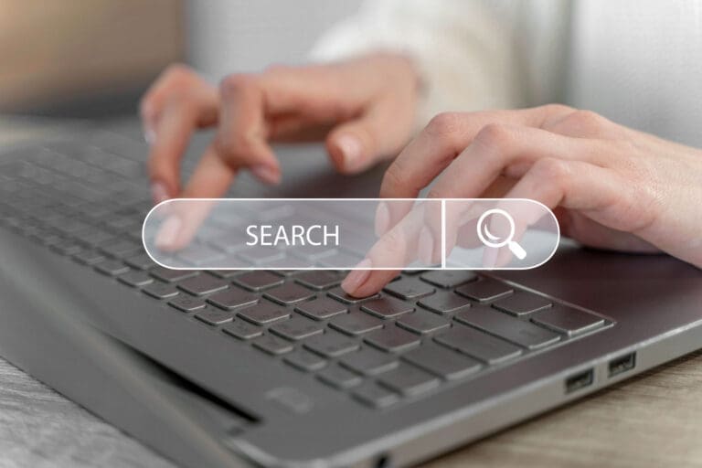 Close-up of hands typing on a laptop keyboard with a transparent search bar overlay and a magnifying glass icon, representing an online search or internet browsing concept.